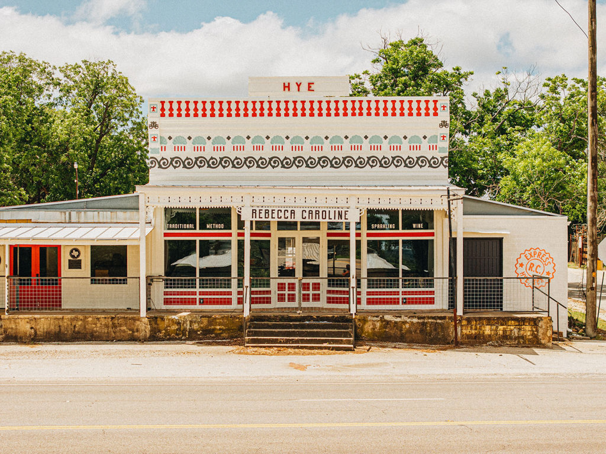 An older building painted white with red and blue accents that says HYE at the top and has a sign that says REBECCA CAROLINE