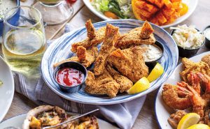 A blue and white shallow dish filled with fried seafood, two dipping sauces, and lemon wedges next to a glass of white wine