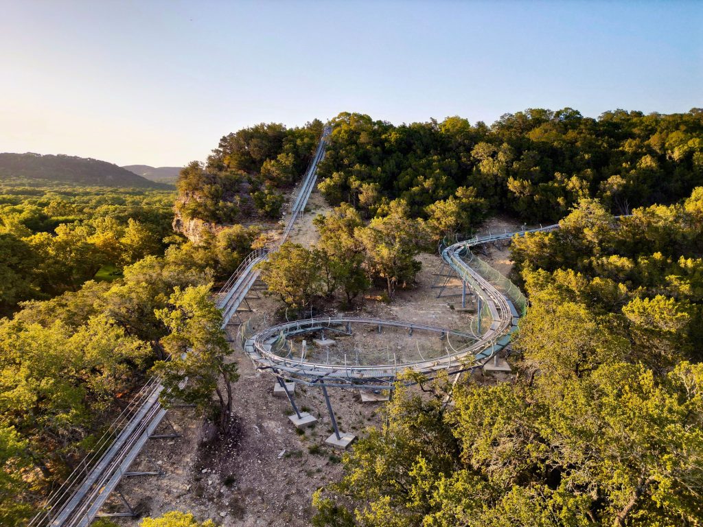 An alpine coaster with a large drop that cuts through a thicket of trees and a loop next to it