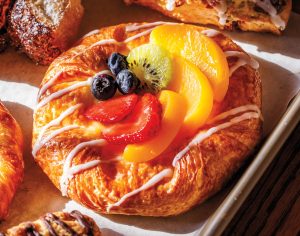 A flaky pastry with white icing drizzled atop and strawberries, kiwi, blueberries, and mango