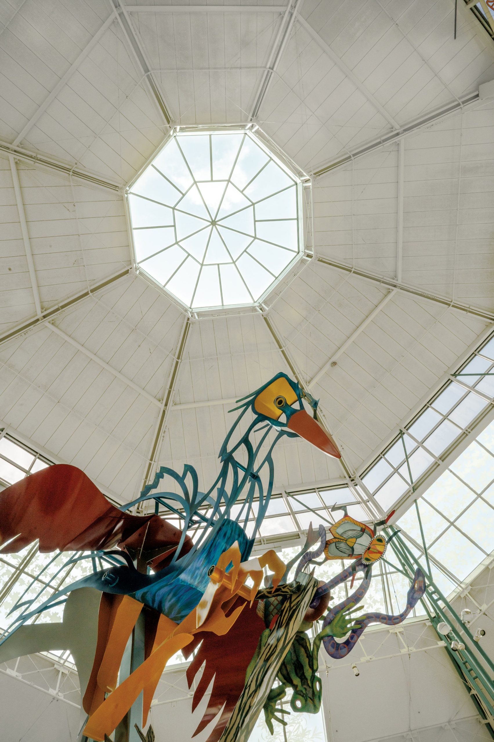 Colorful statues of a bird, a snake, a frog, and other animals under a skylight