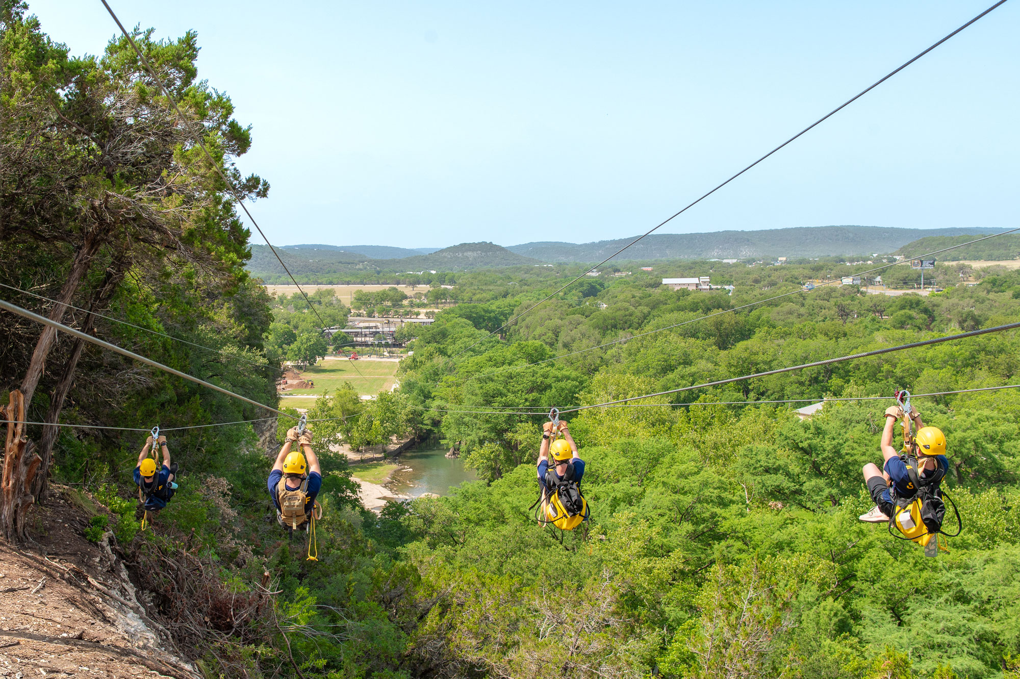 Four people zip-lining downward toward a forest