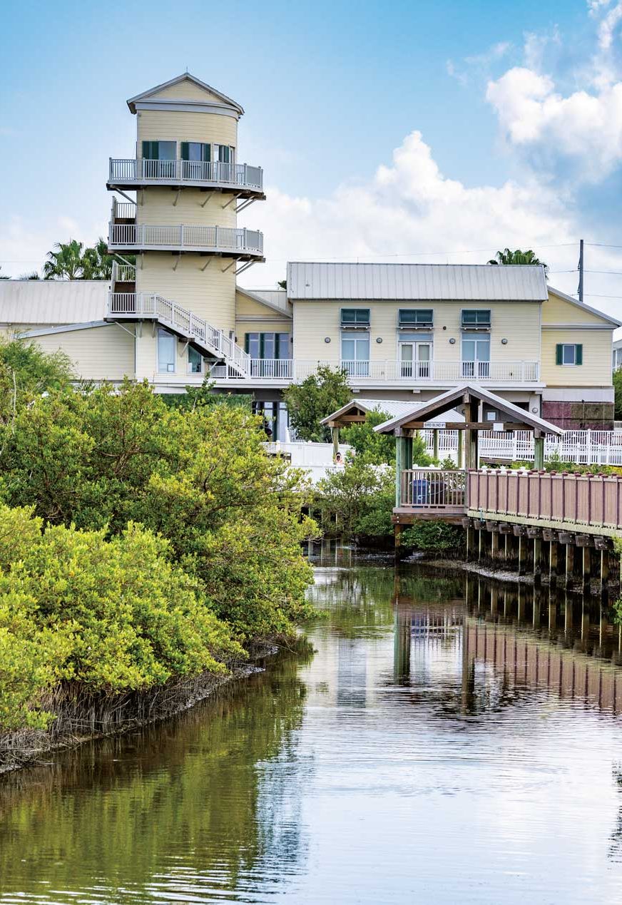 A tall lighthouse-esque building framed by a body of water and a dock