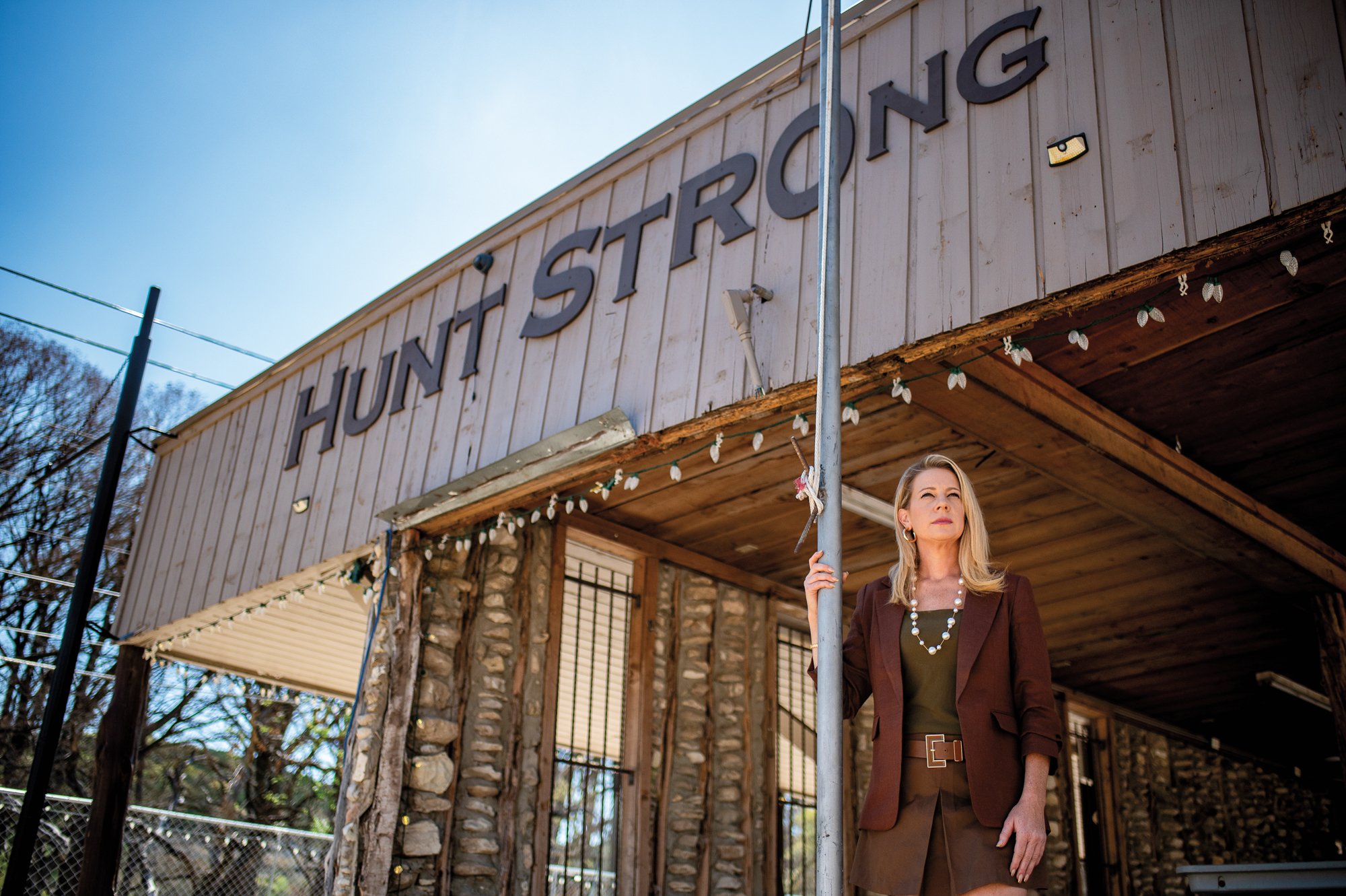 A woman in a brown suit stands outside a storefront that reads "Hunt Strong"