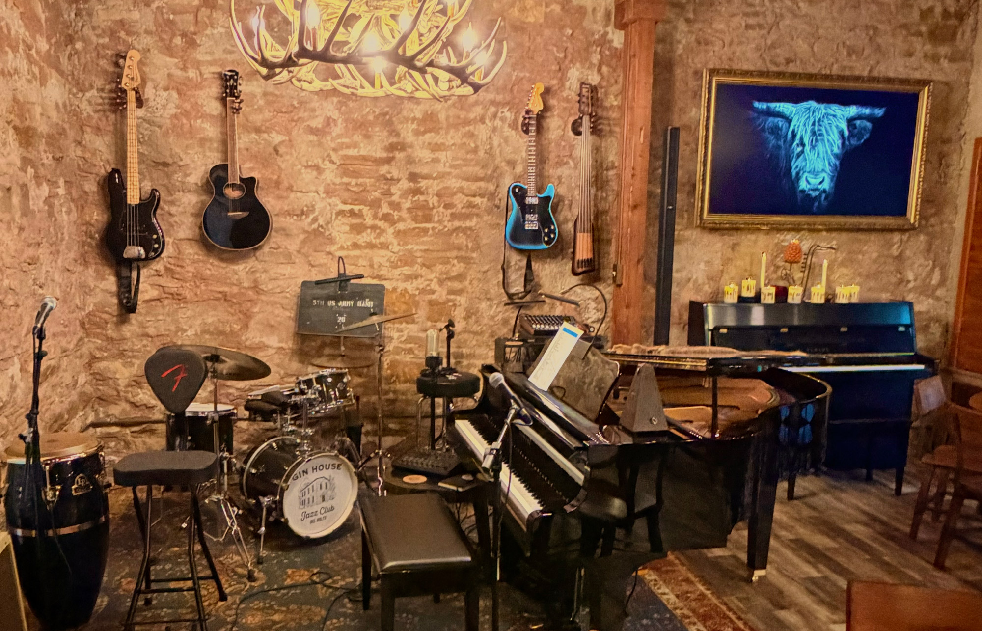 Guitars hanging on a brick wall above a drum kit, a piano, and other musical instruments