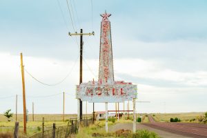A faded blue sign with a star on top that reads Stardust Motel on the left side of a deserted road