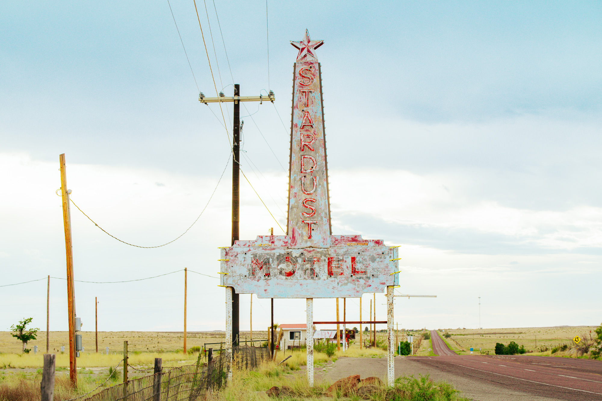 A faded blue sign with a star on top that reads Stardust Motel on the left side of a deserted road