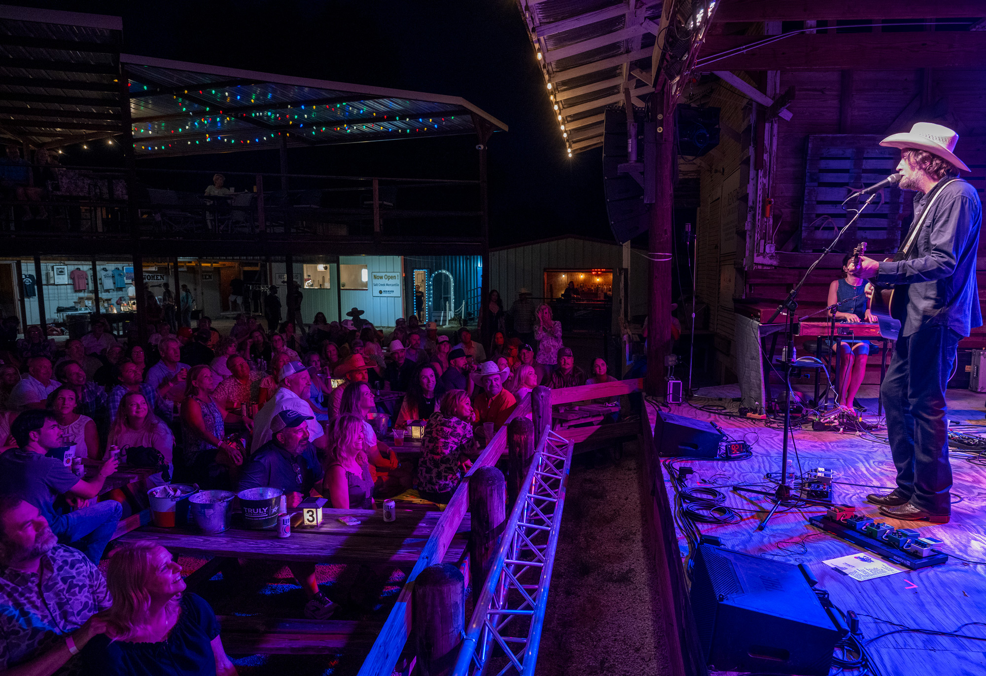 A man in a cowboy hat playing guitar in front of a large audience at night