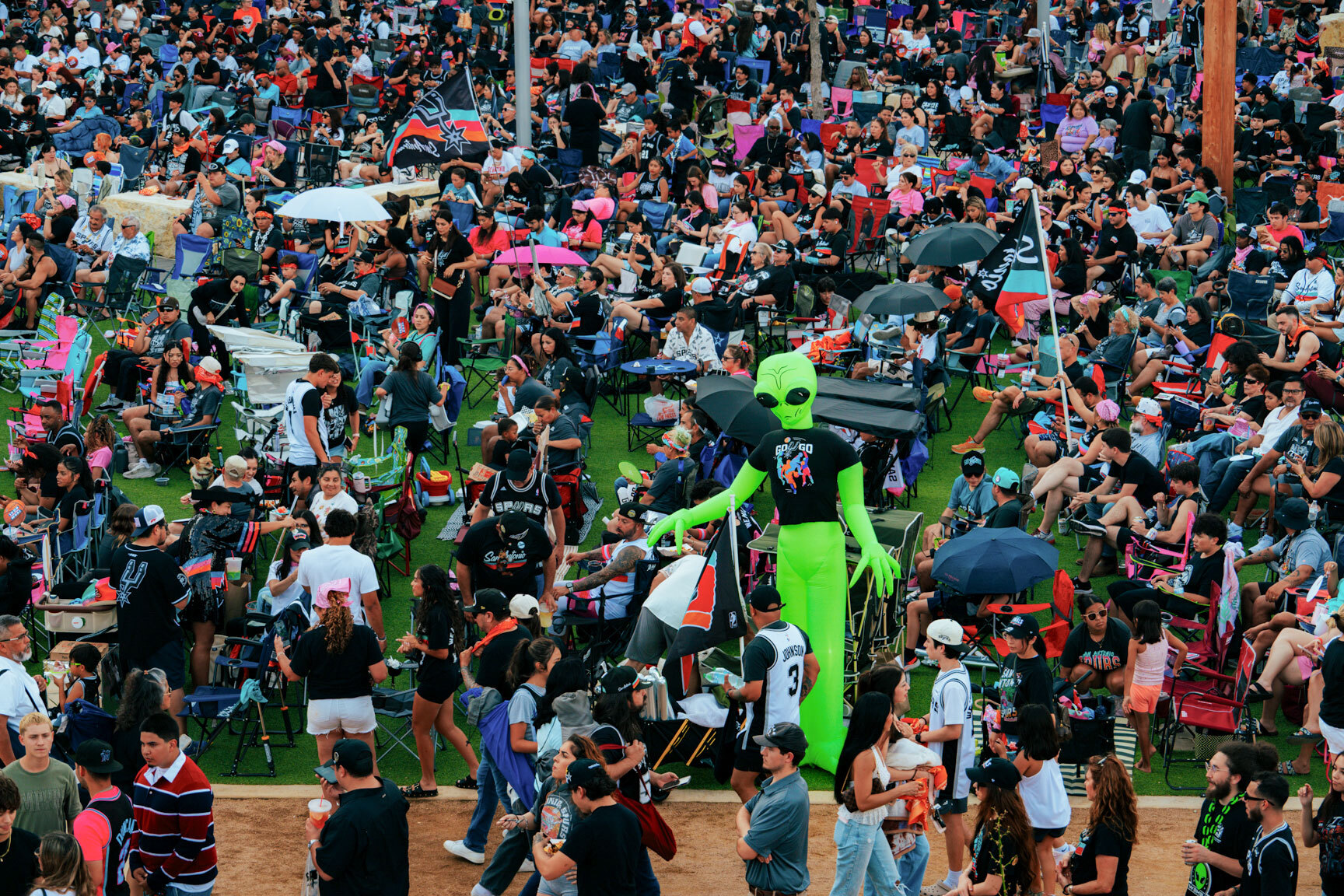 A large group of Spurs fans on a lawn, with a large inflatable green alien in the middle wearing a Spurs shirt