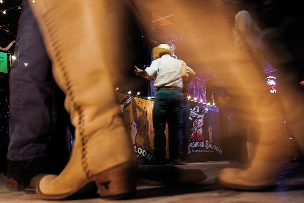 Two brown boots in the foreground with two people dancing behind them