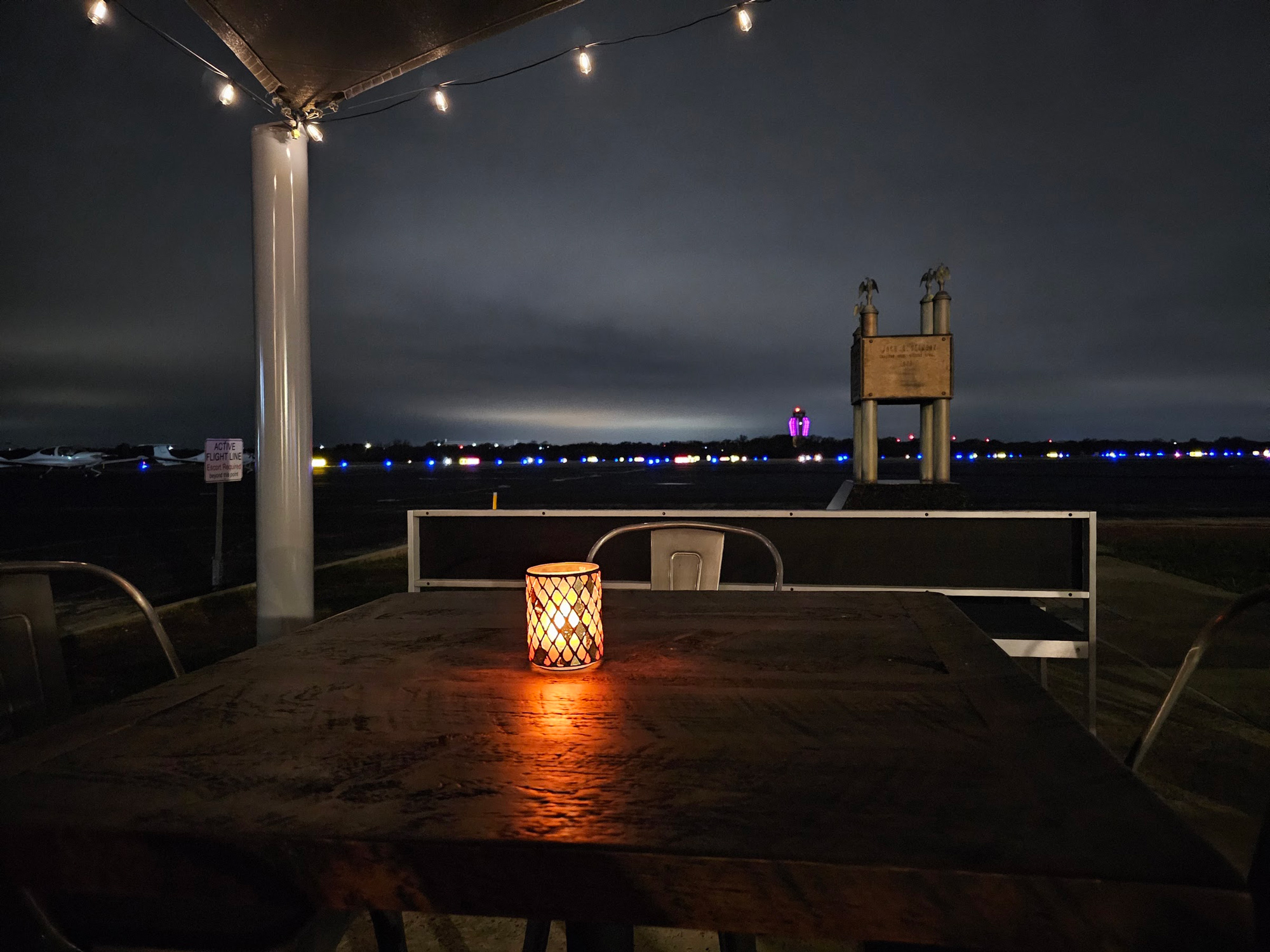 A wooden table with a lit candle in the middle at night near a tarmac