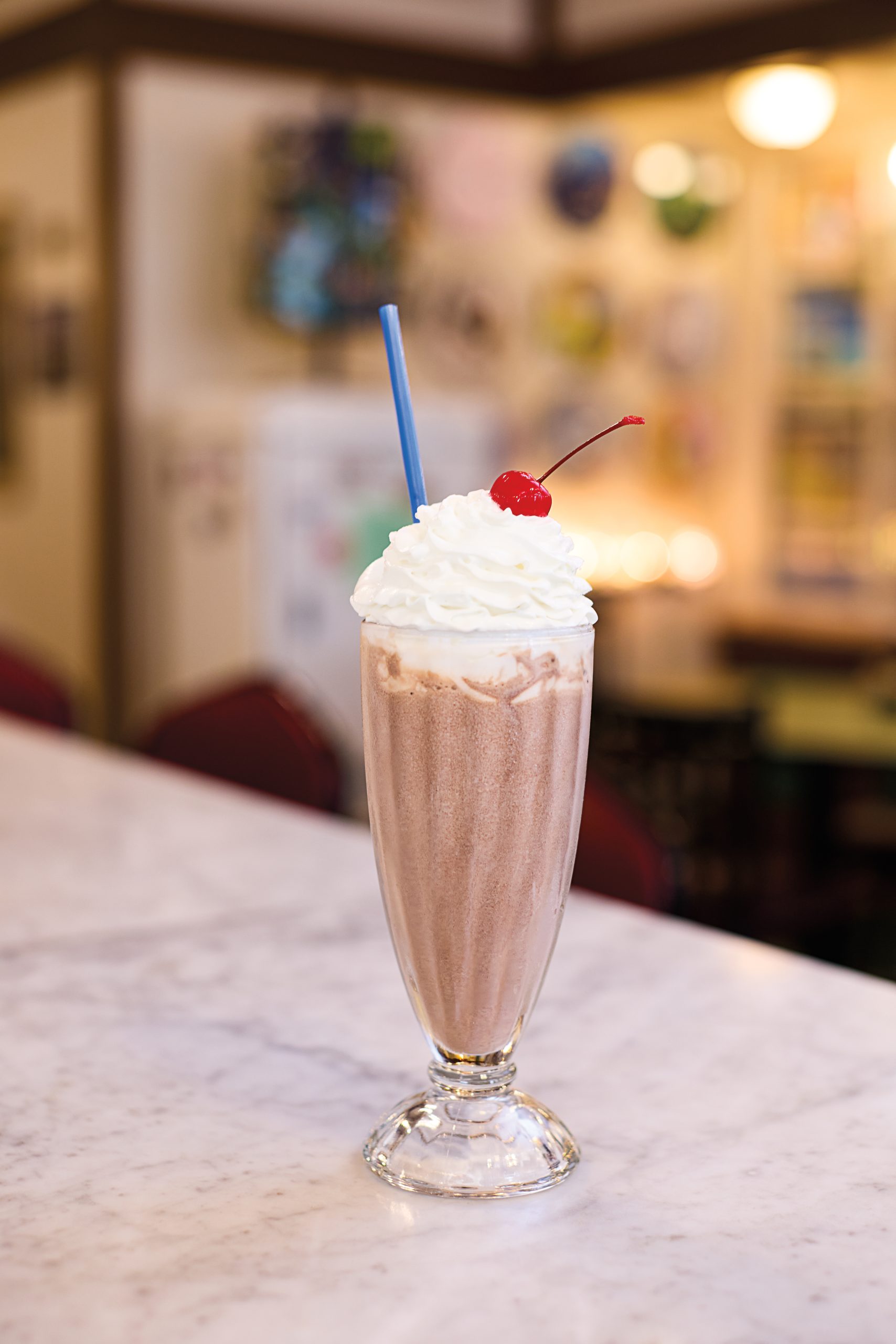 A chocolate milkshake topped with a cherry and whipped cream in a classic glass on a counter