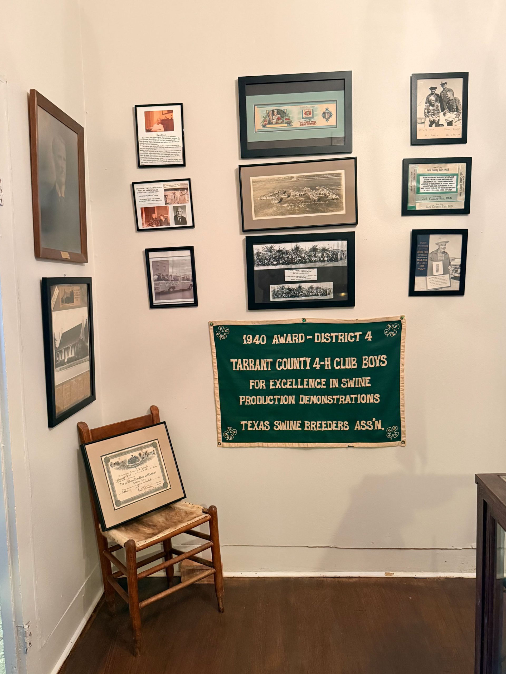 Multiple framed items are displayed on a wall, along with a green banner that says, "Tarrant County 4-H Club Boys" and a small wooden chair in the corner.