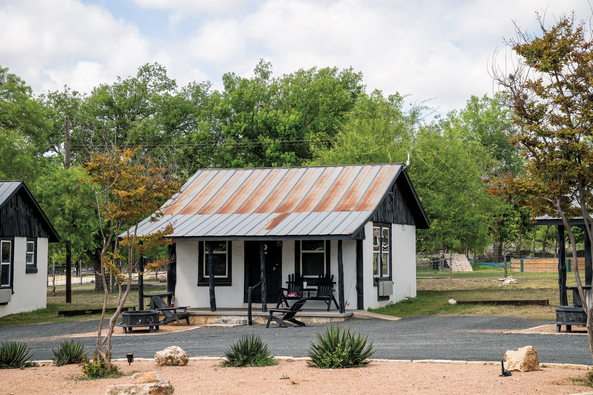 A small, white cabin with black accents and black chairs on its porch.