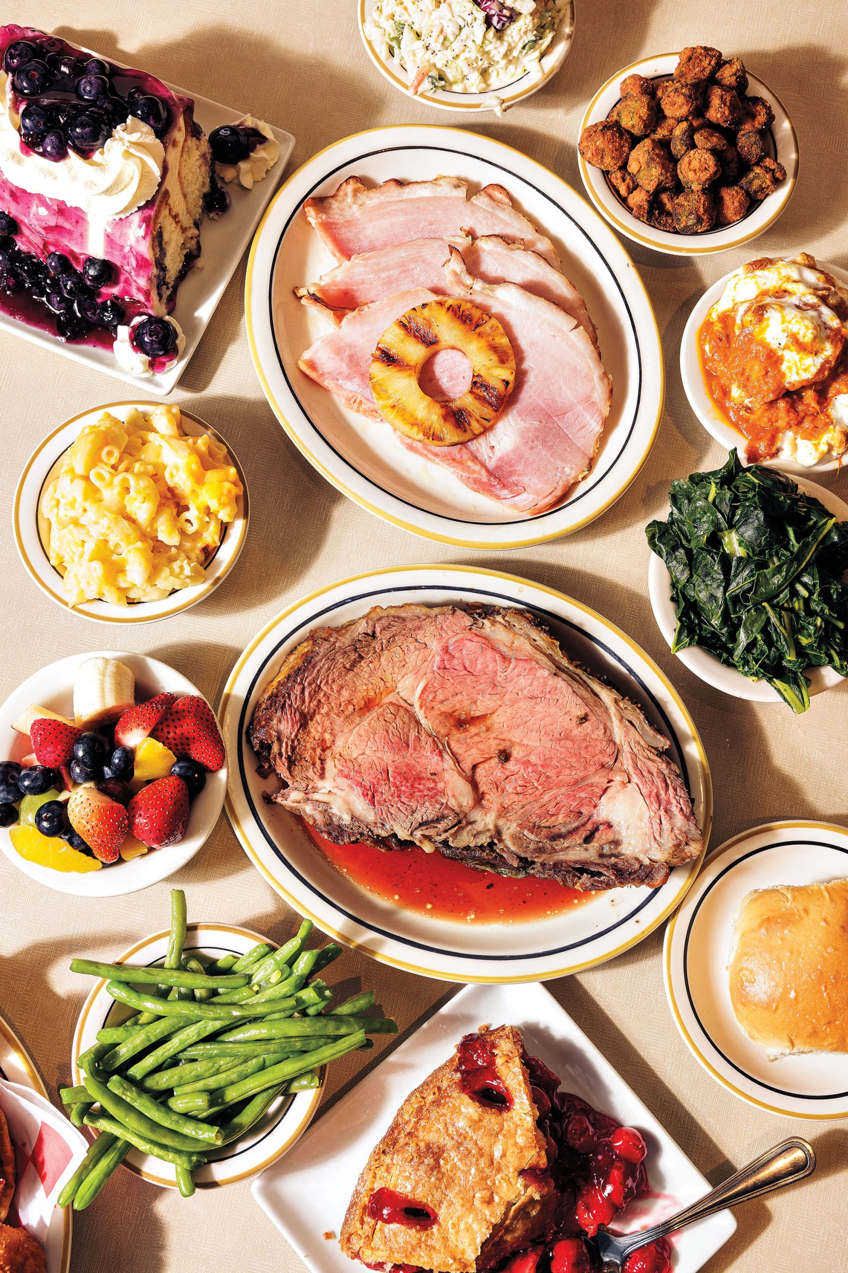 Various plates of vibrant-colored Southern food, including ham, steak, green beans, side dishes, fruit, cake, and pie.