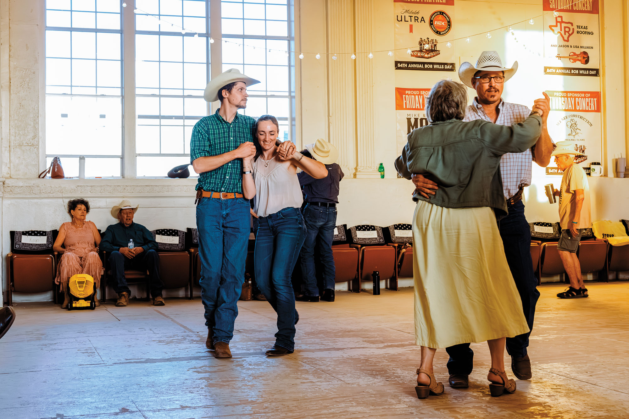 Couples in Western wear dance the two-step in a dance hall