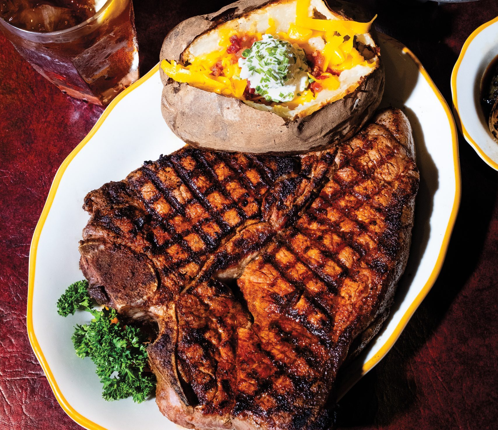 A large grilled steak served on a plate with a cheesy baked potato