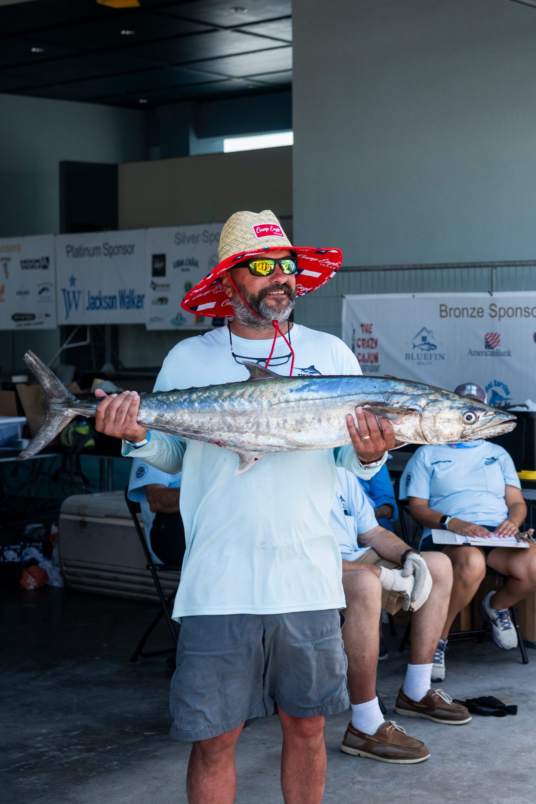 A man in a straw bucket hat holds a large fish
