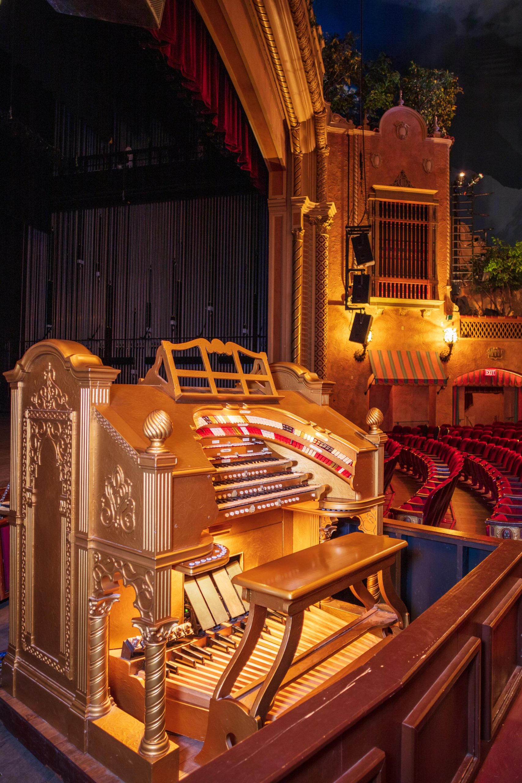 A gold organ and a wooden bench near a stage and some red seats inside a theater