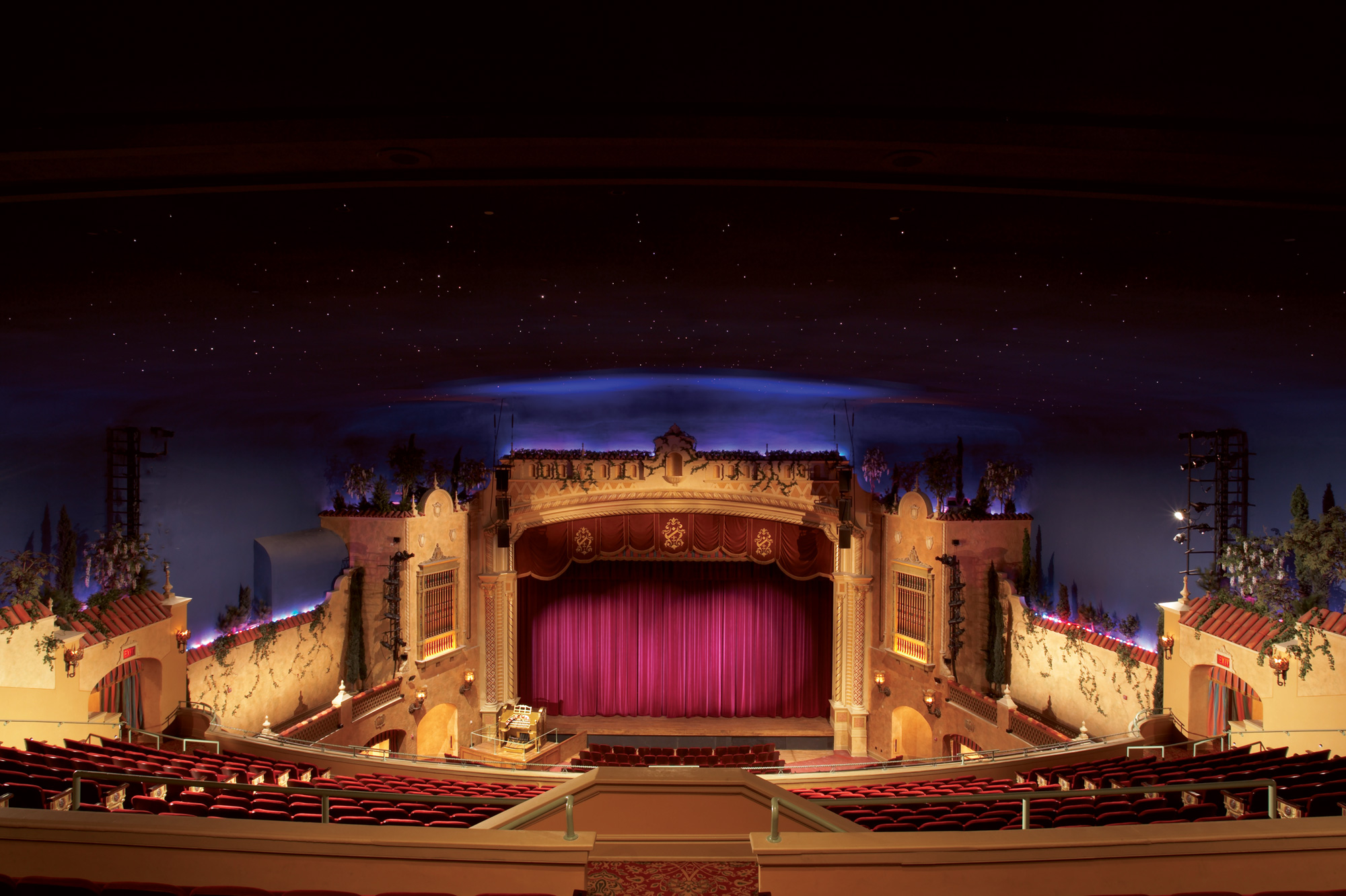 A large theater with painted stars on the ceiling, red seats, a closed red curtain on the stage