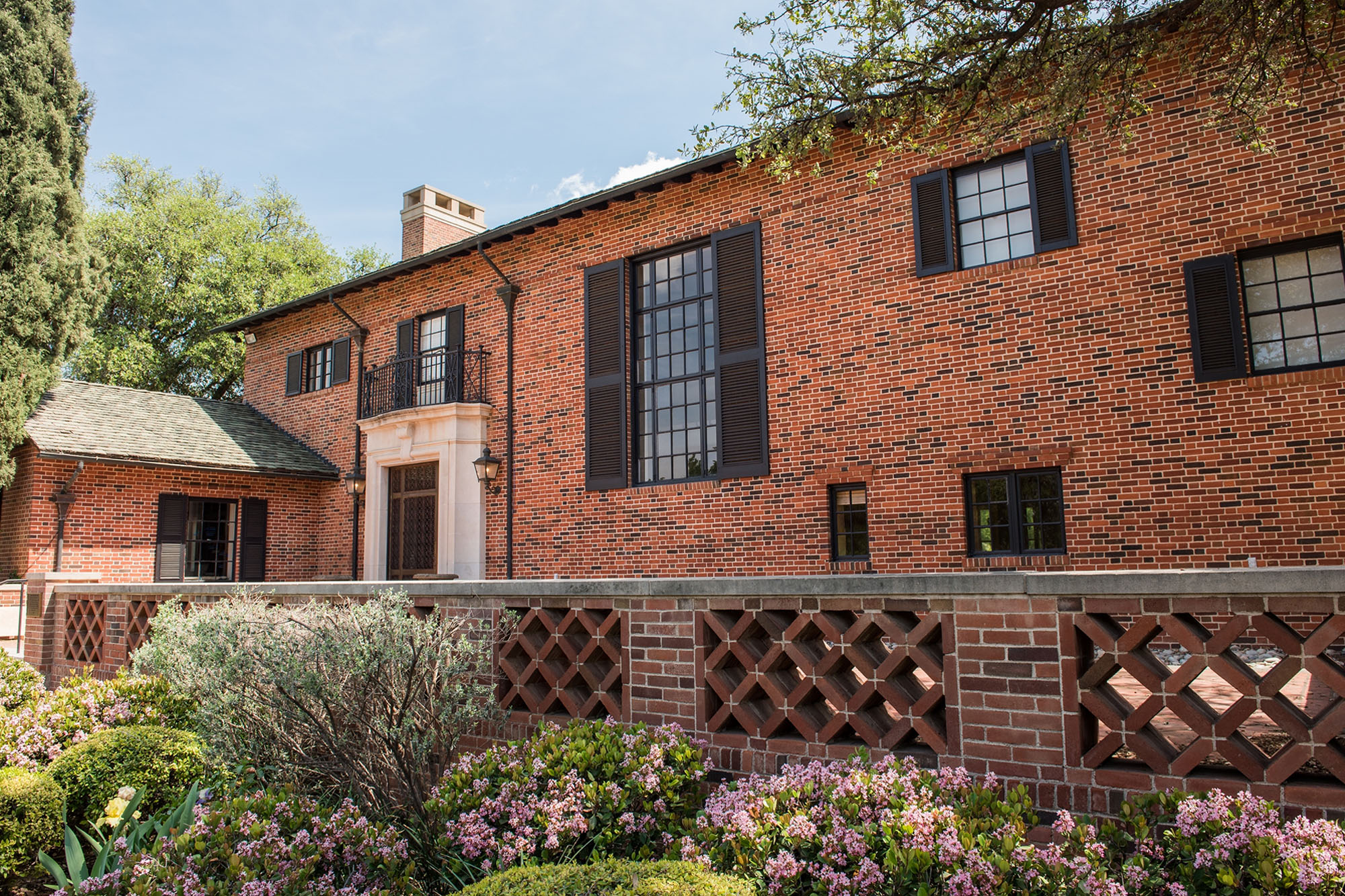 A large red-brick estate during the daytime, fronted with vibrant foliage and bushes.