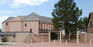 A tan building with dark wood accents and a slanted shingle roof with a sign in front of it that reads "The Globe Theatre"