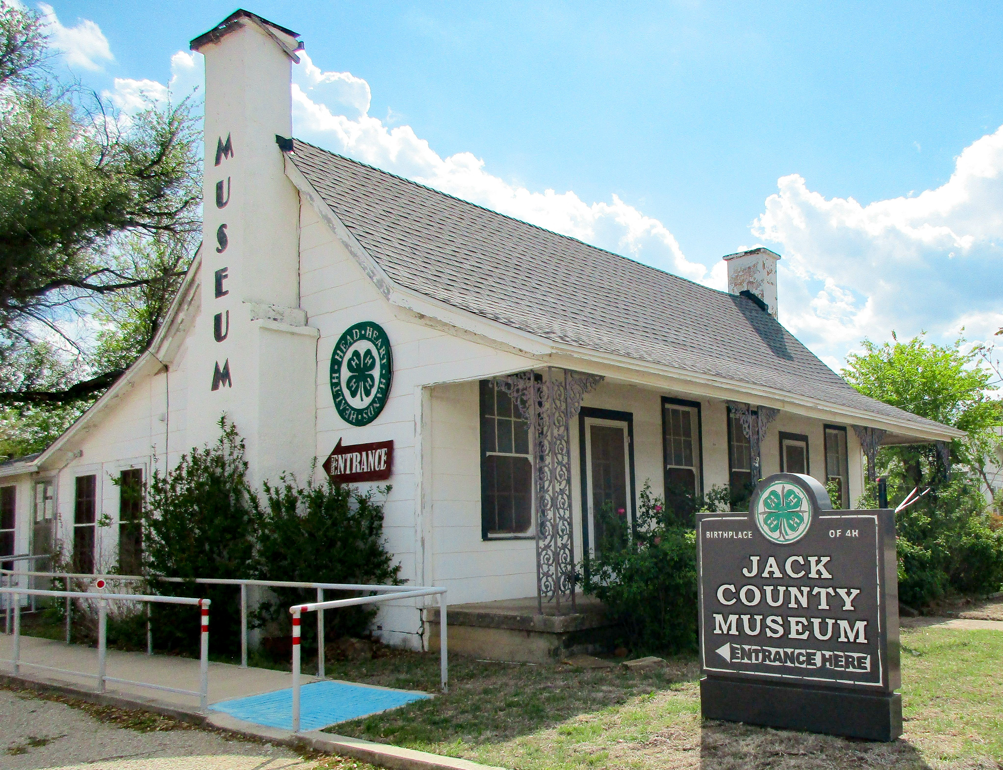 The Jack County Museum, a small white building with a dark roof and chimney, with a 4-H logo and "Entrance" sign on the wall.