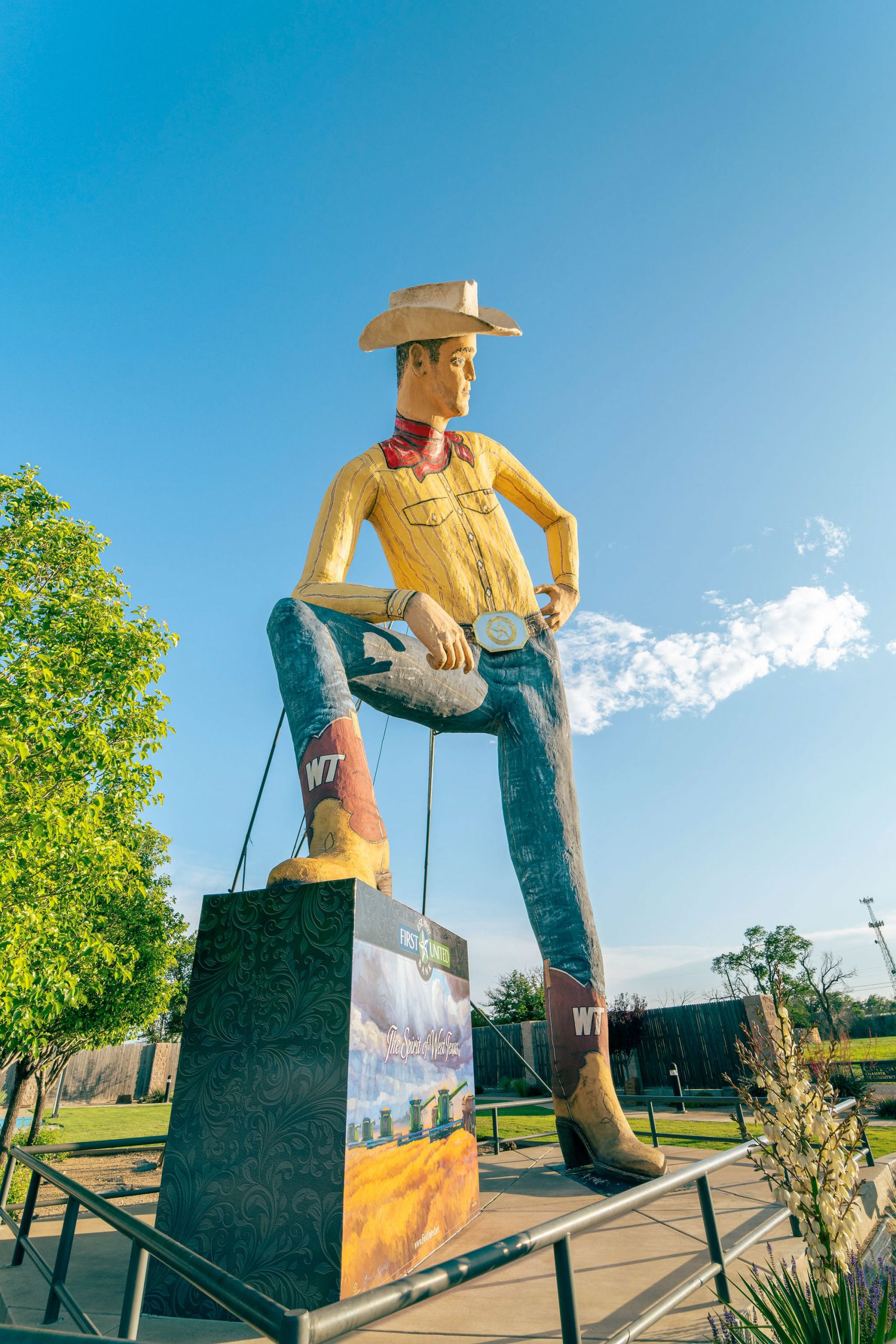 A giant cowboy statue posing with one boot up on a sign.