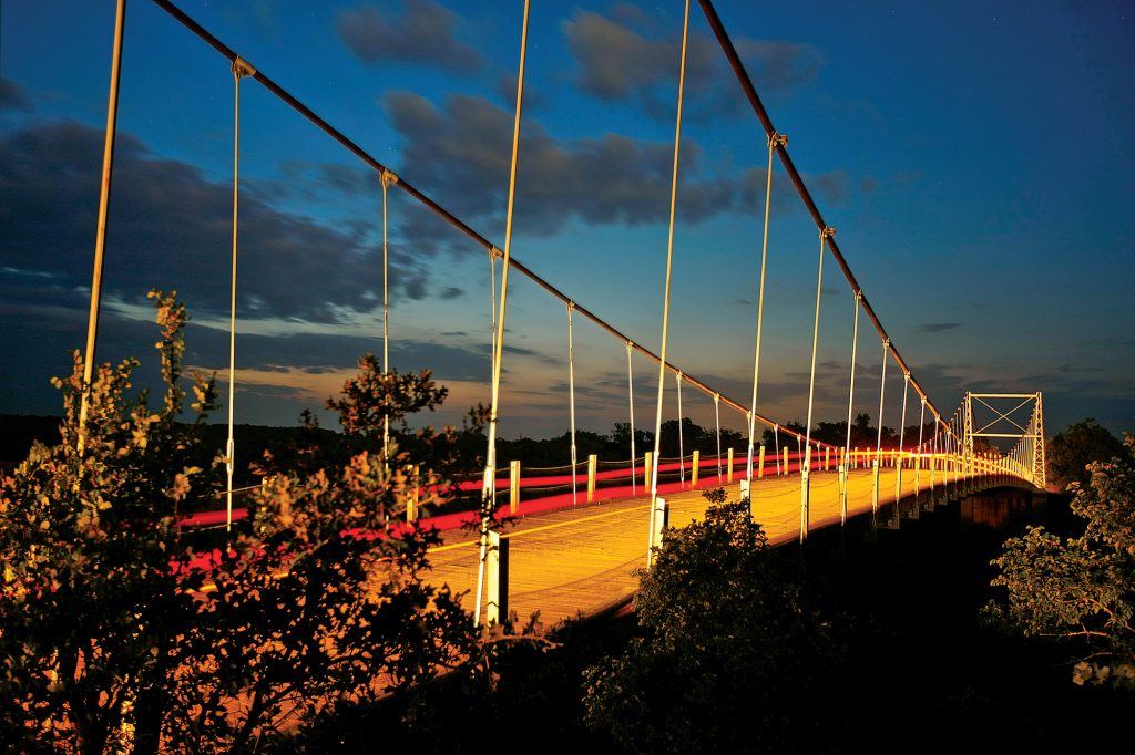 A suspension bridge made of wire and wood illuminated by orange lighting