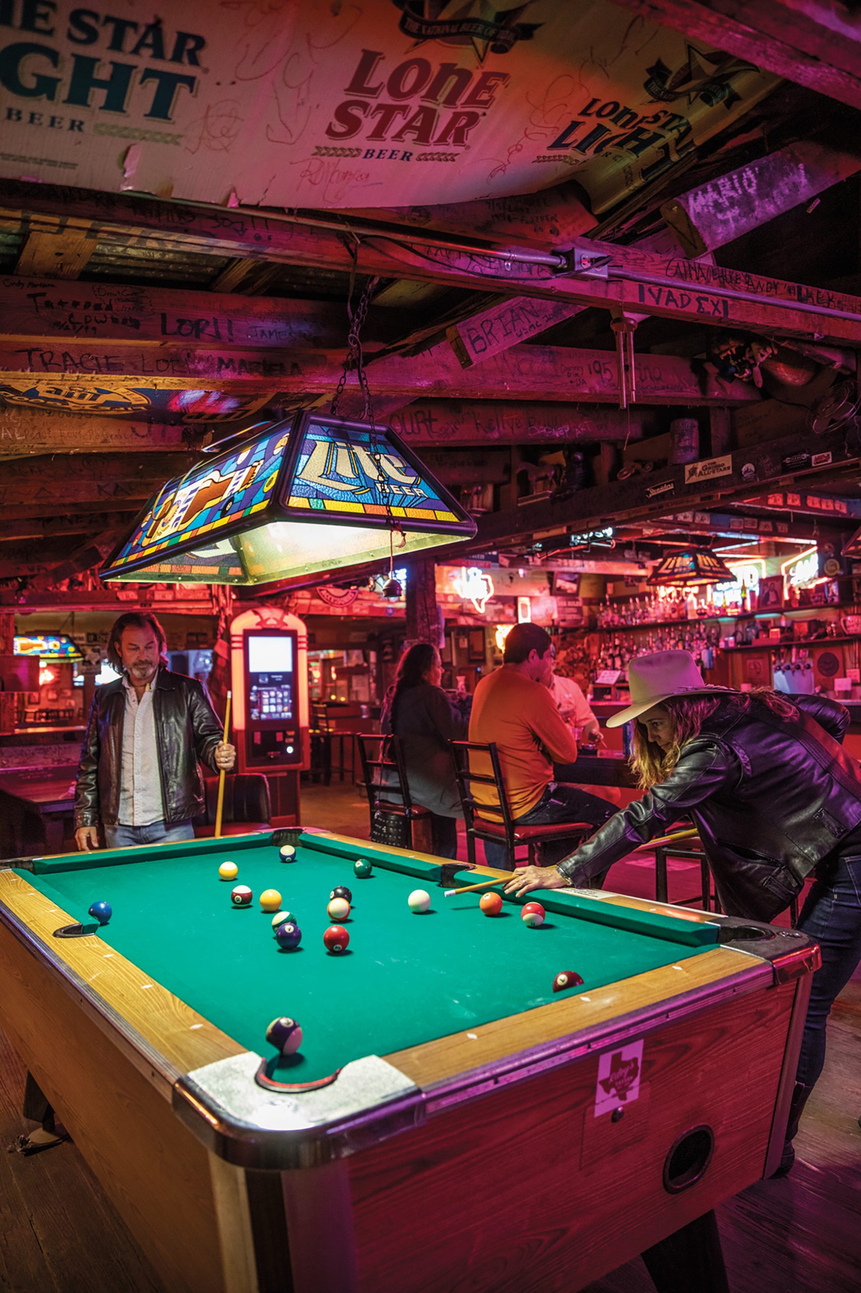 People shoot pool around a pool table in a bar