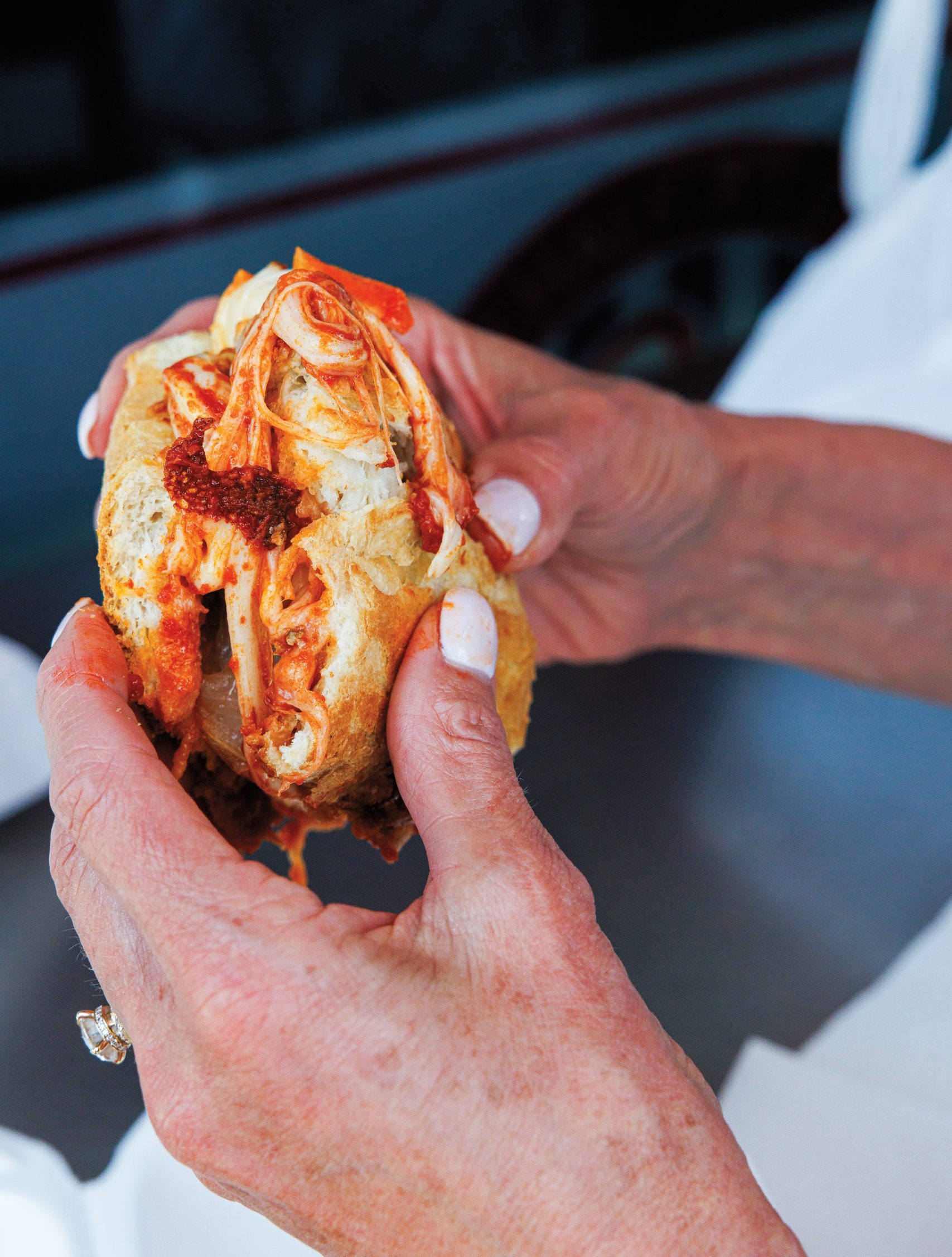 A person's hands holding a chicken Italiano sub with melted mozzarella