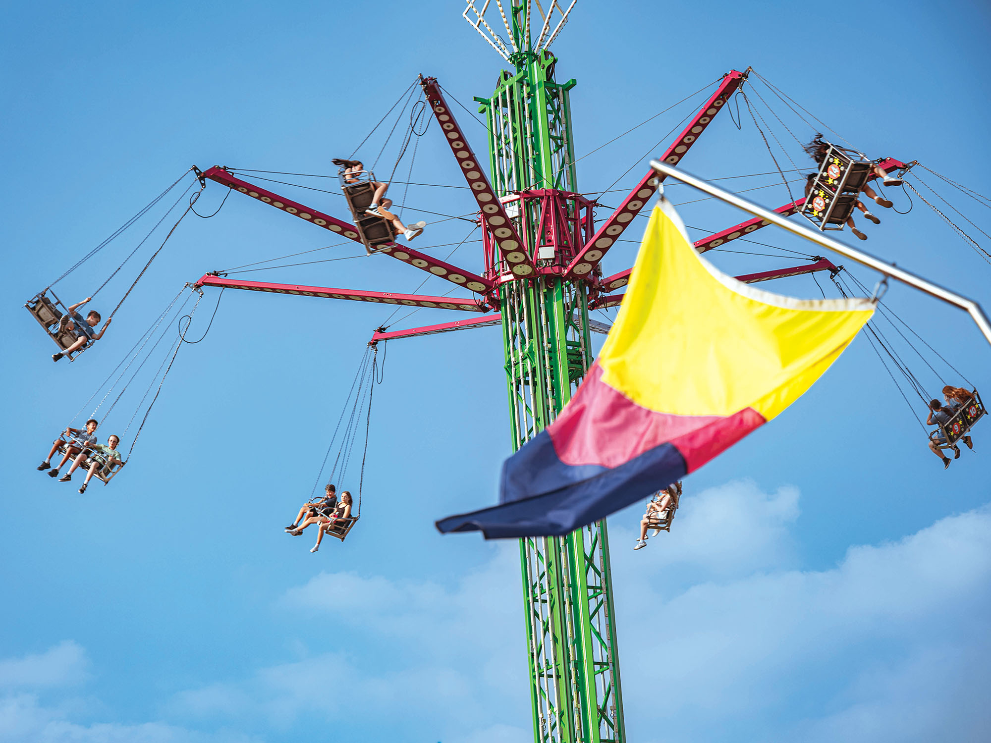 A spinning amusement ride featuring a bright green column and rotating red structure, from which swing seats for passengers are attached.