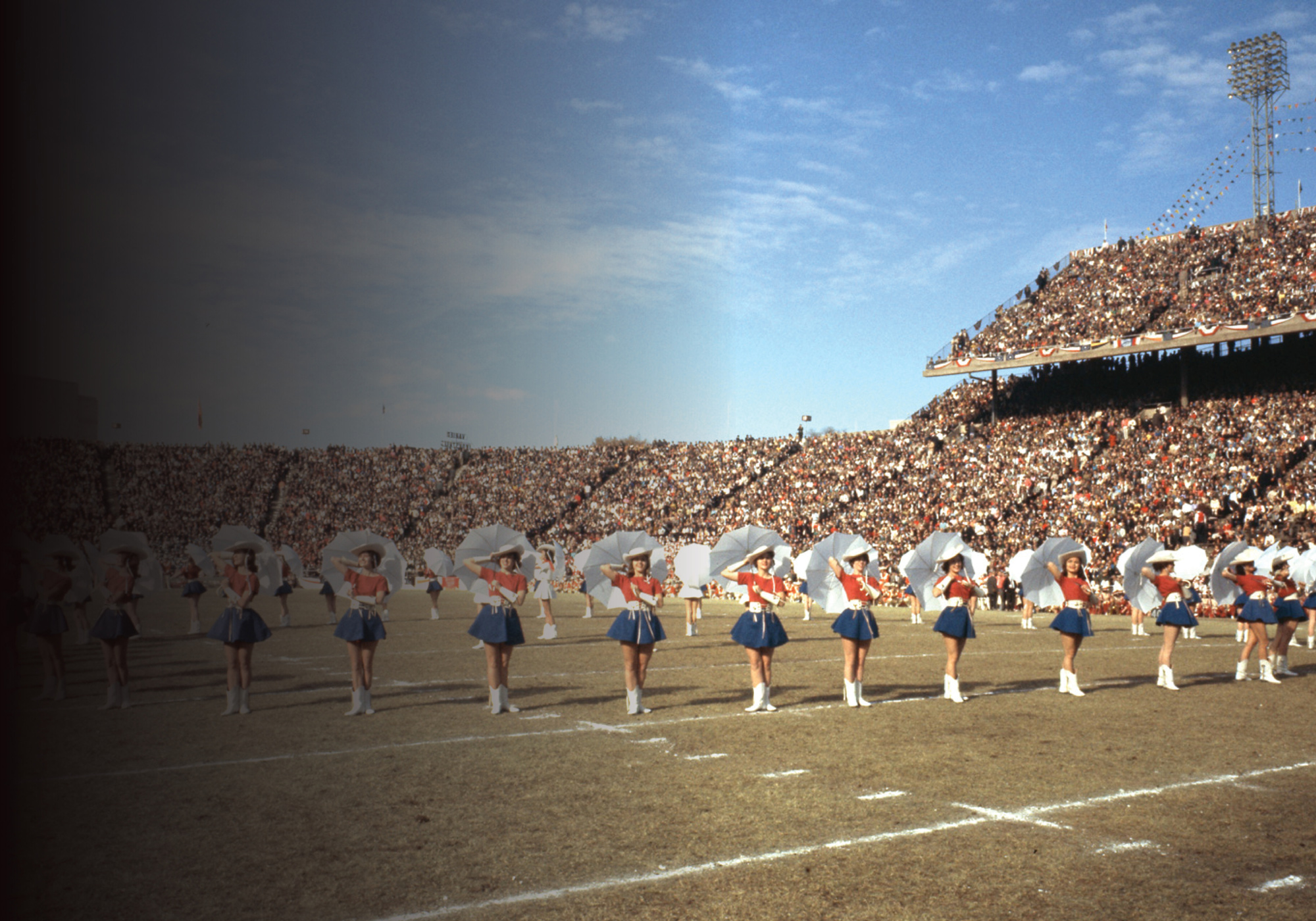 A drill team dressed in red, white, and blue on a football field in a packed outdoor stadium