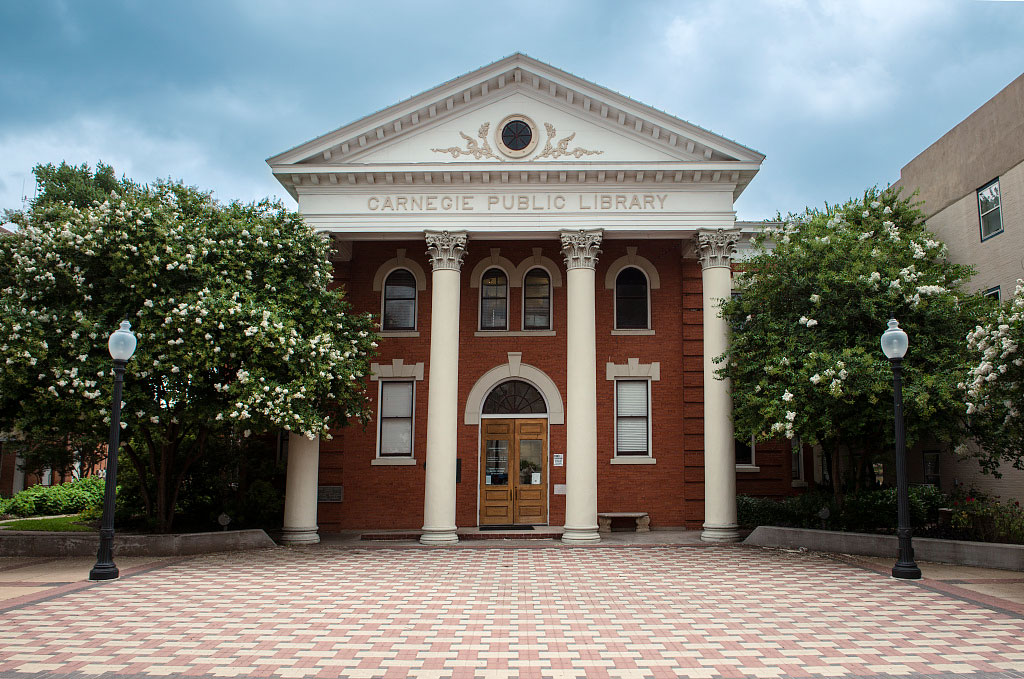 The Carnegie History Center, a red brick building with four white columns and a white triangular pediment, is in the center, with a basketweave-patterned brick sidewalk in front of it.