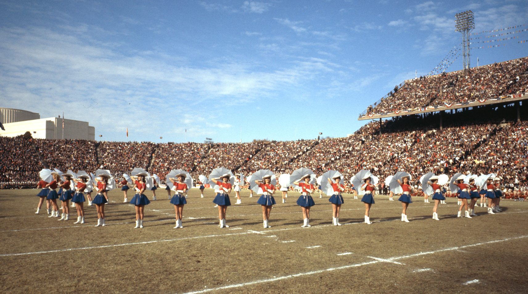 A drill team dressed in red, white, and blue on a football field in a packed outdoor stadium