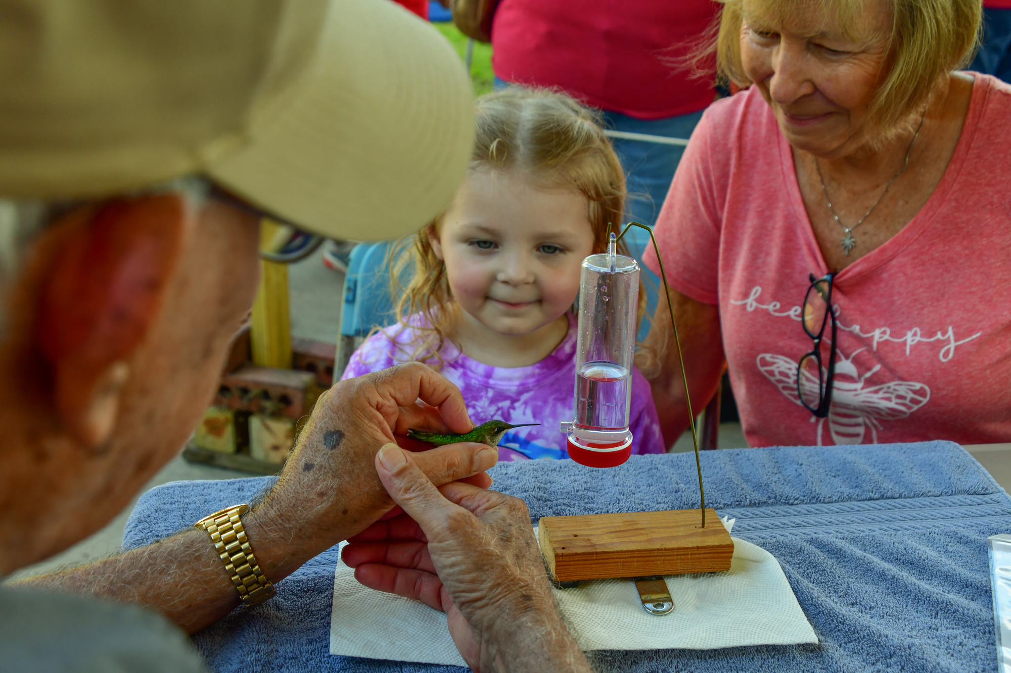 A man holding a hummingbird in front of a young girl and a woman