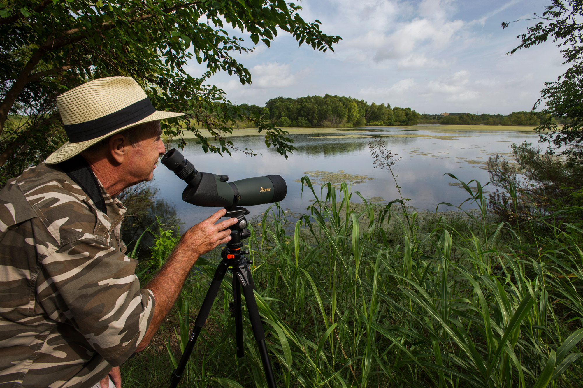 A man in a tan hat with a dark band looks through monoculars in a bird blind