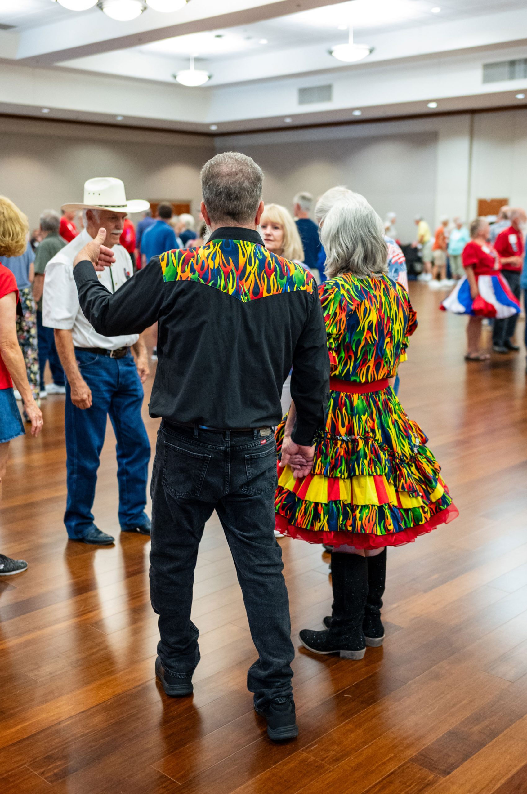 A man and woman in outfits with a similar colorful fire motif, his on a black button down shirt and hers on a full dress