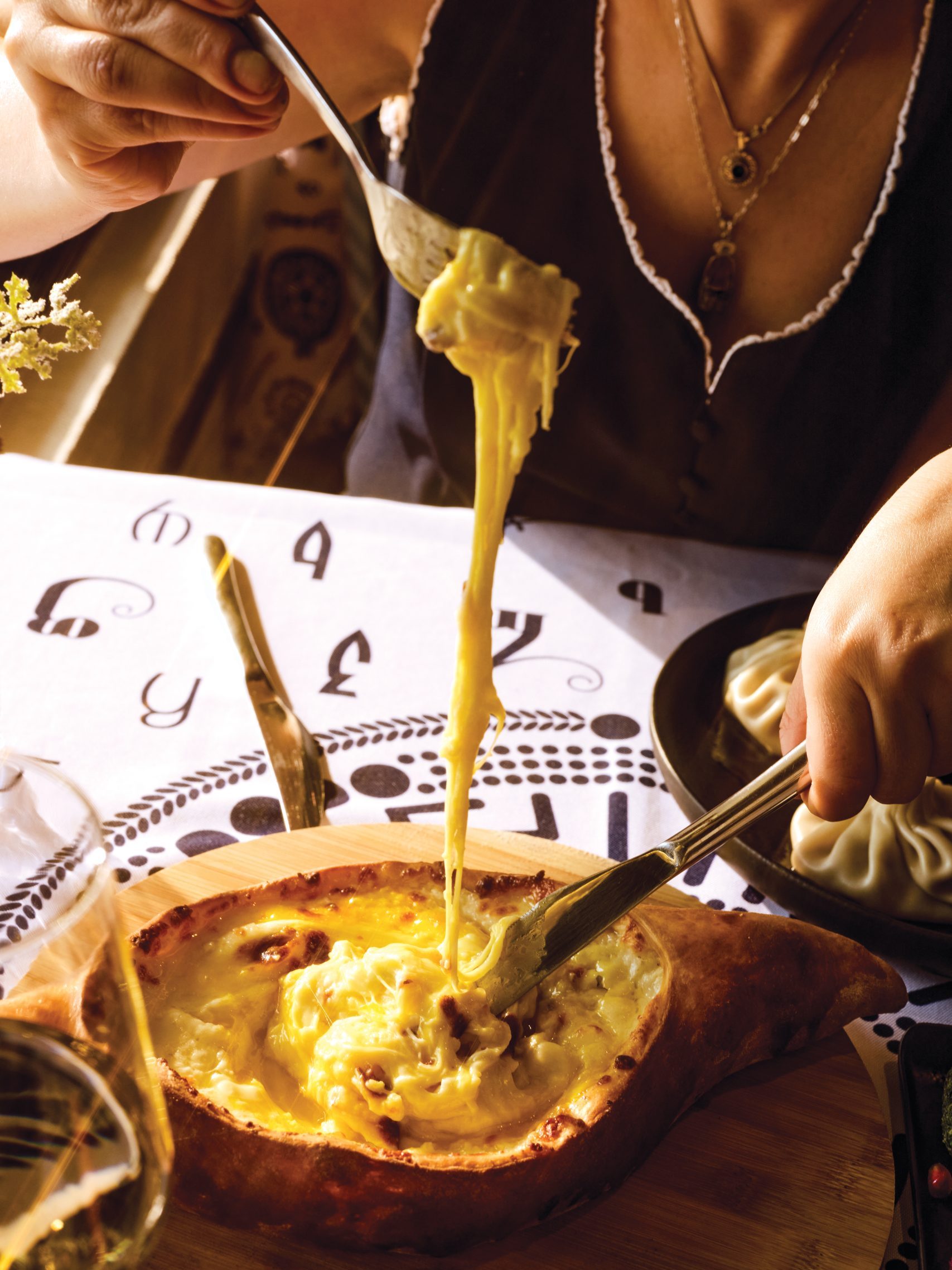 A woman pulls a string of cheese using a fork from a cheese-filled boat-shaped bread bowl.