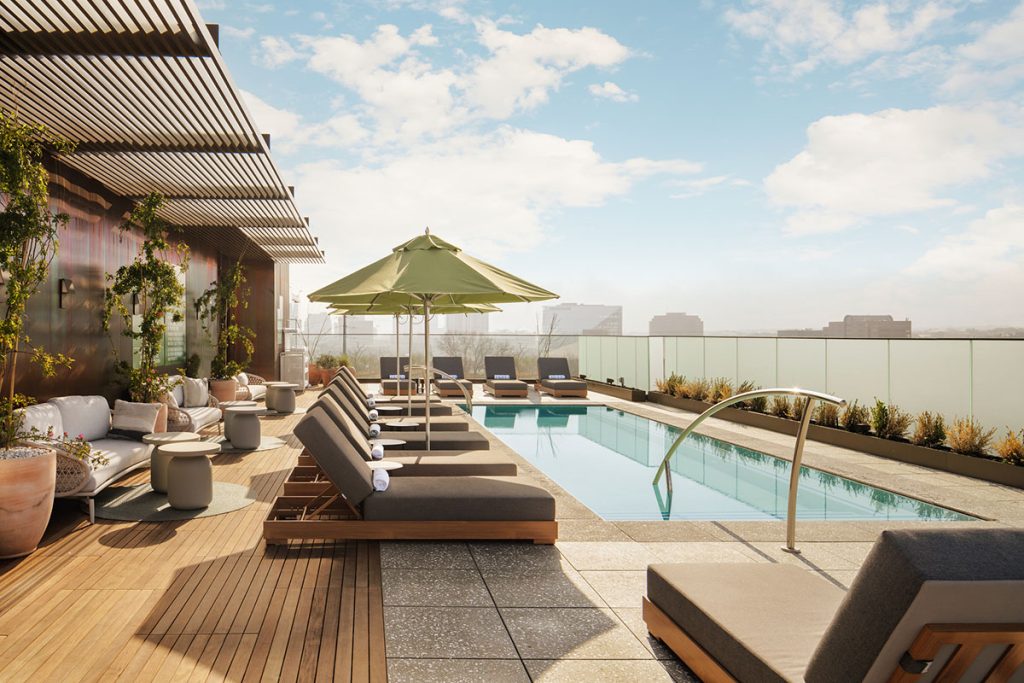 Reclining chairs line a rooftop pool overlooking a cityscape and sunny sky
