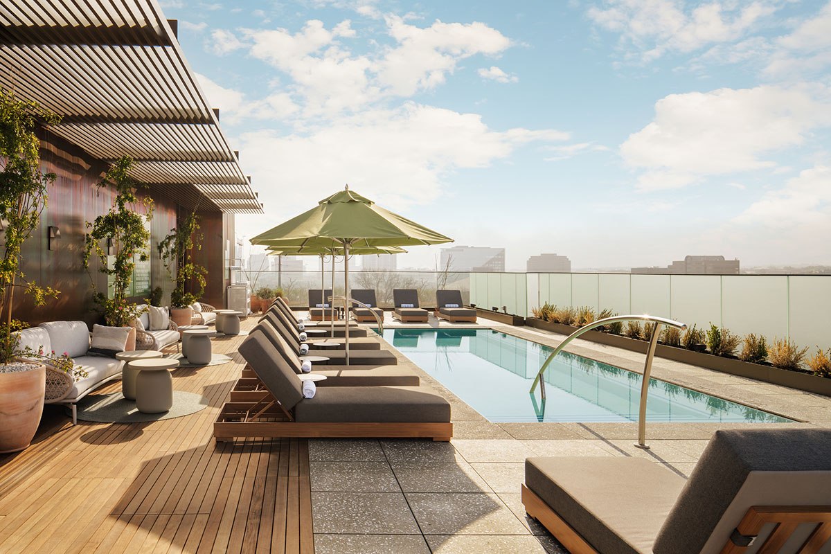 Reclining chairs line a rooftop pool overlooking a cityscape and sunny sky