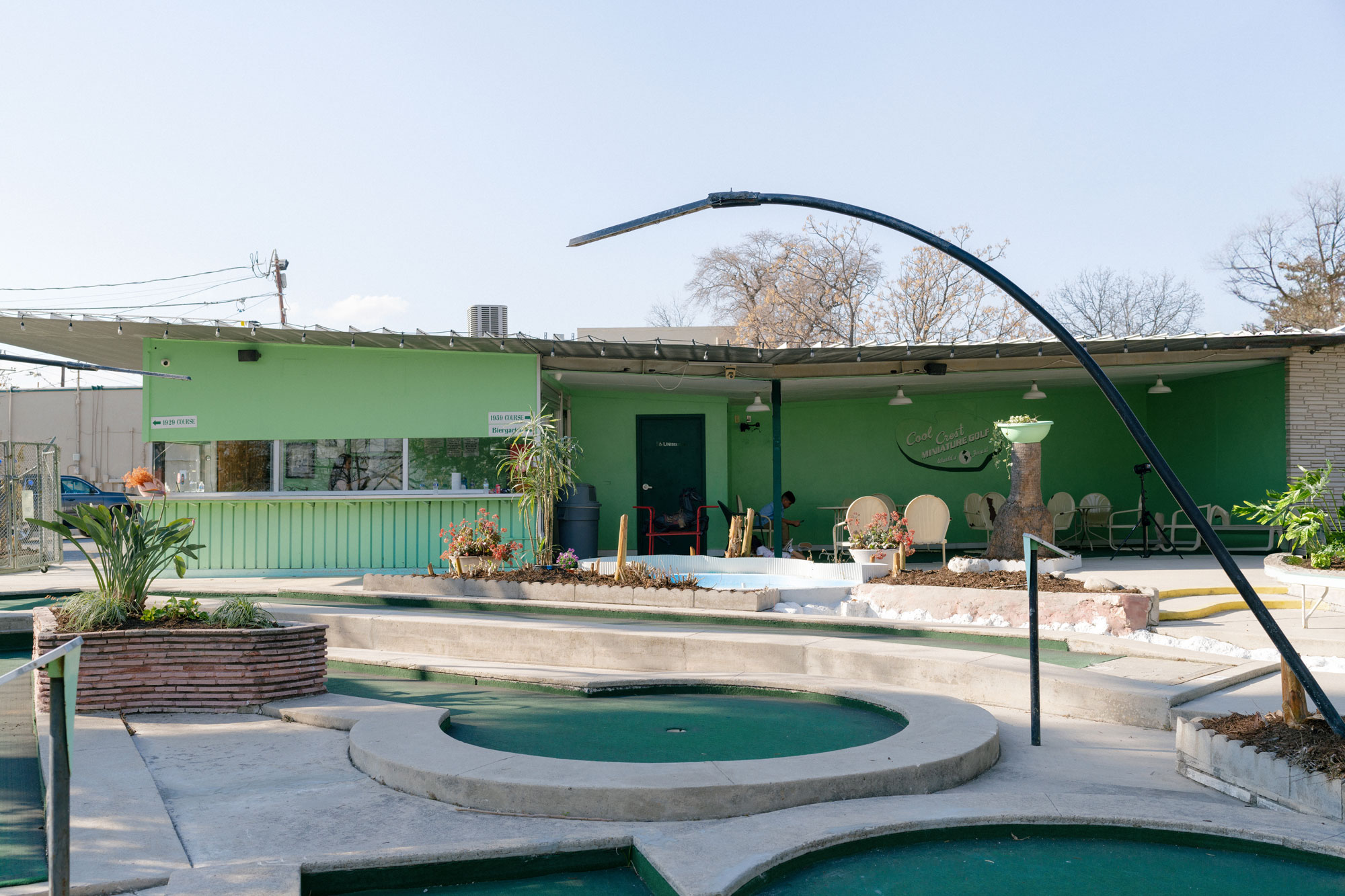 Mini golf holes with green carpet are in front of the light green main building of Cool Crest Miniature Golf.