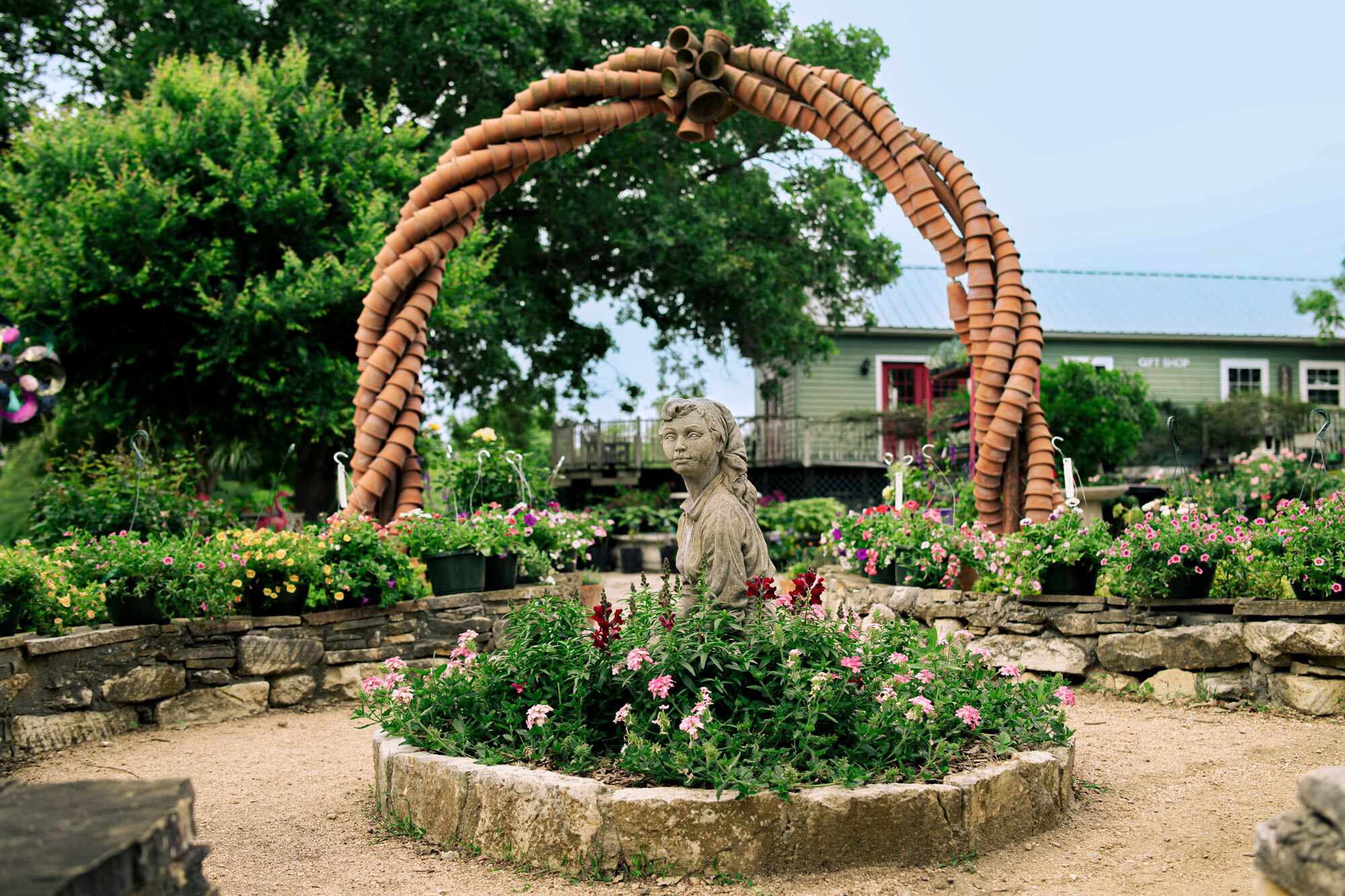 Pink roses in a round planter with a statue of a woman in the middle in front of a long, winding arch