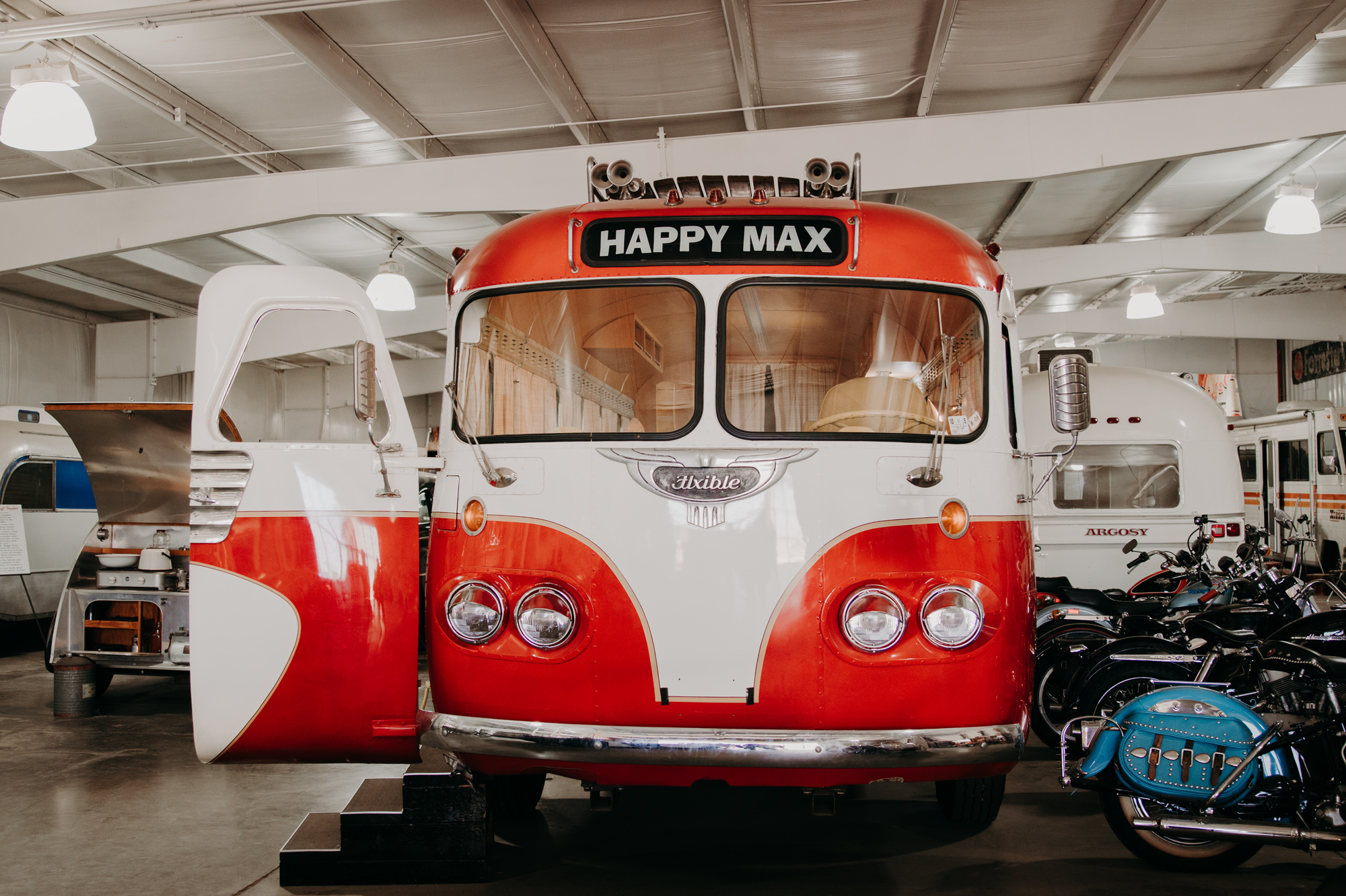 A red retro RV with a label that reads "Happy Max" located inside a large facility