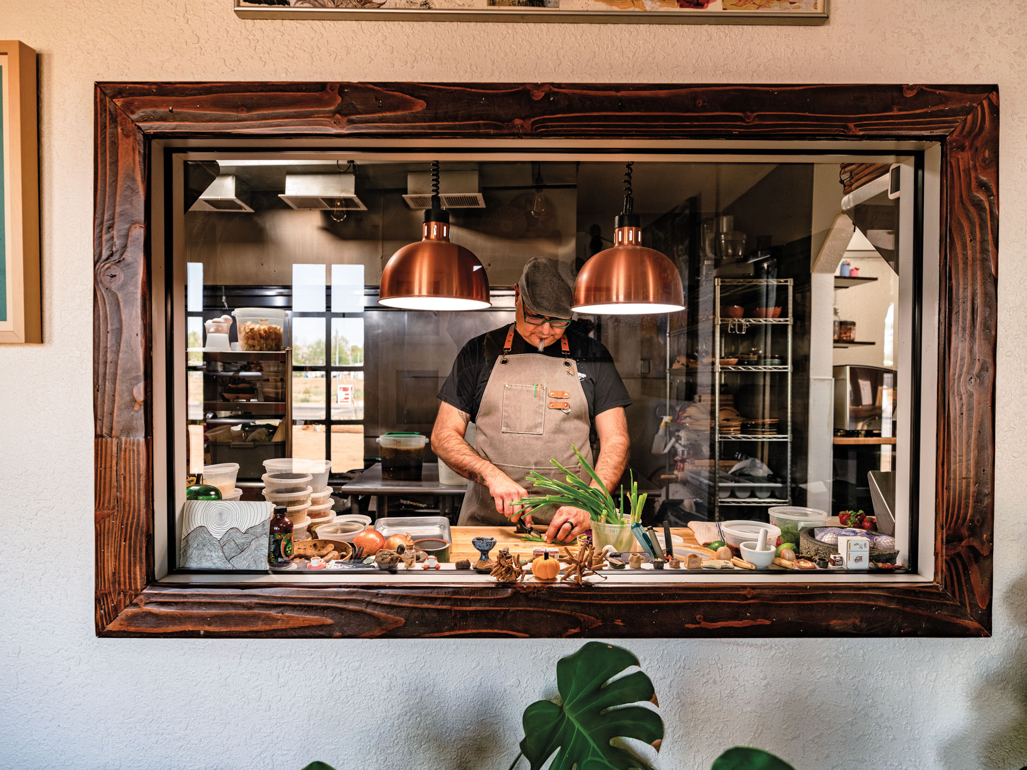 A man in glasses, a cap, and apron prepares food in an industrial kitchen.