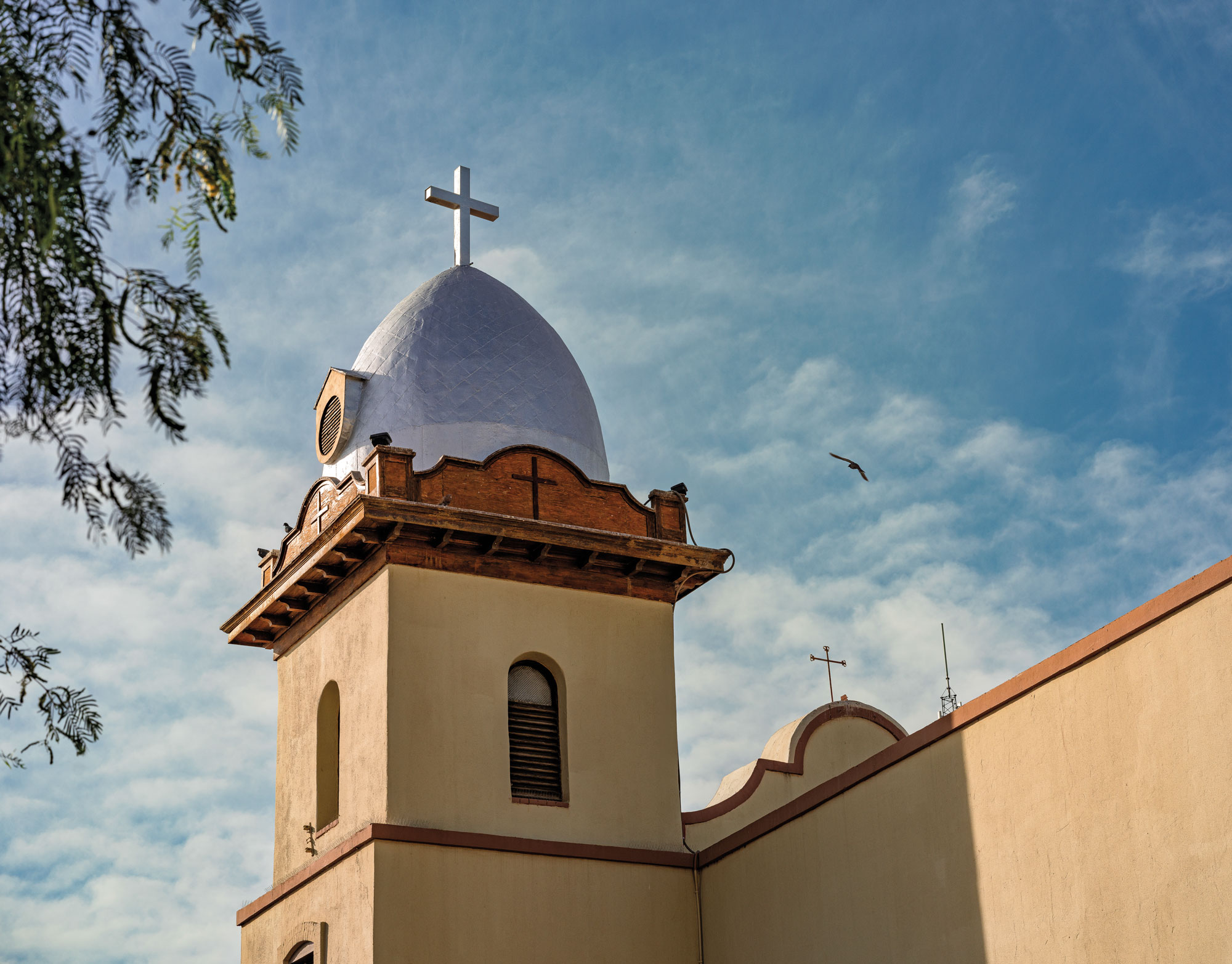 The top of a beige and blue adobe mission against the sky.