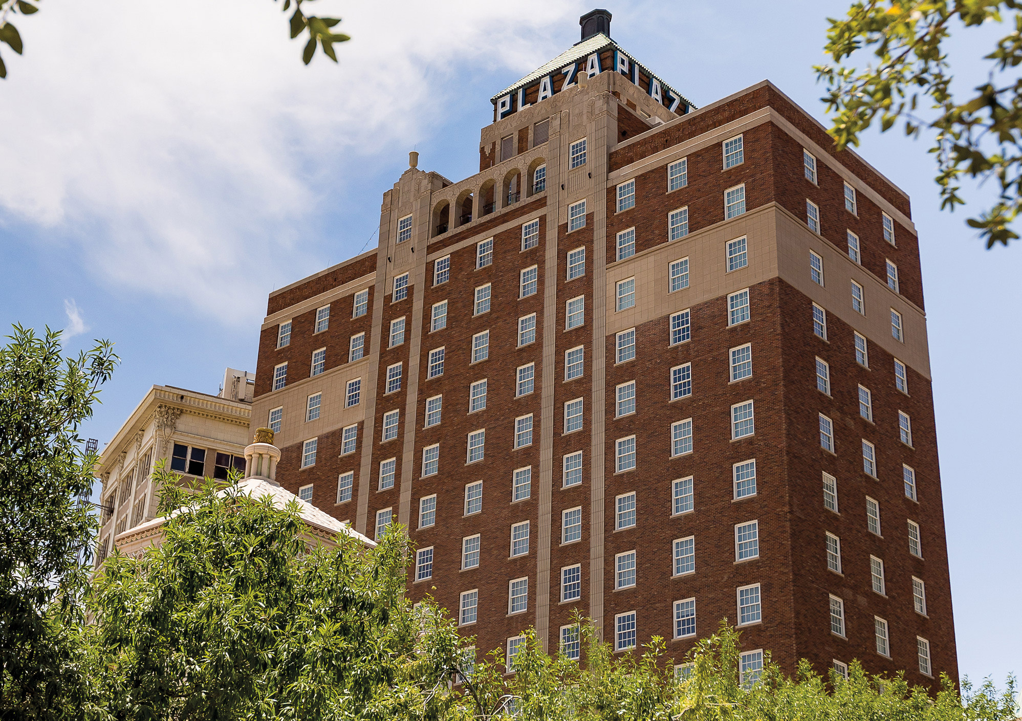 A large brick building that says Plaza on the top floor behind greenery