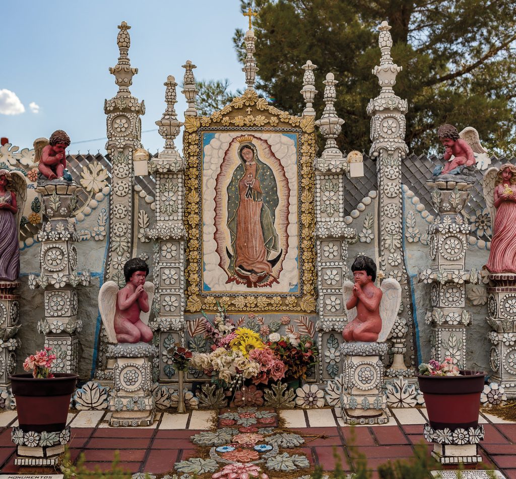 An ornate facade of a house with multiple columns and two praying angels with flowers on the red tiles