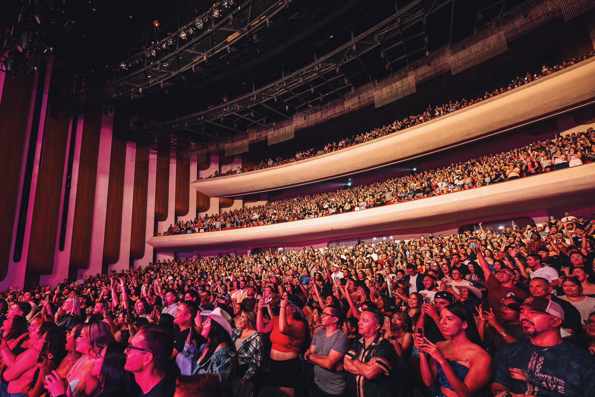A large, enthusiastic crowd standing in a theatre, with two balconies filled with people