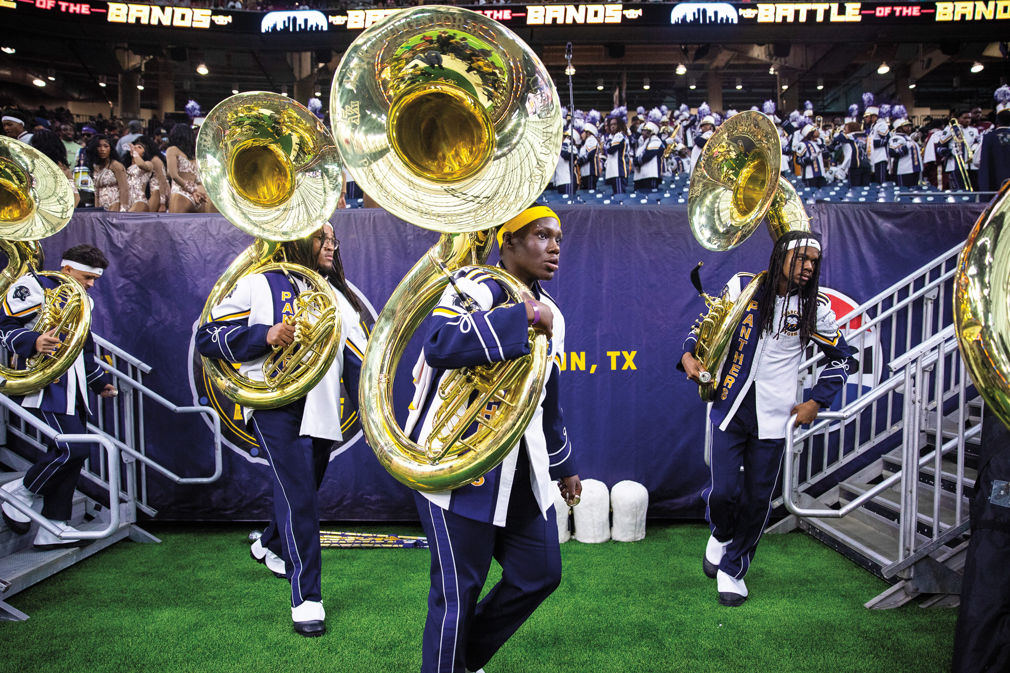 Tuba players in a marching band walking onto the field in a large stadium